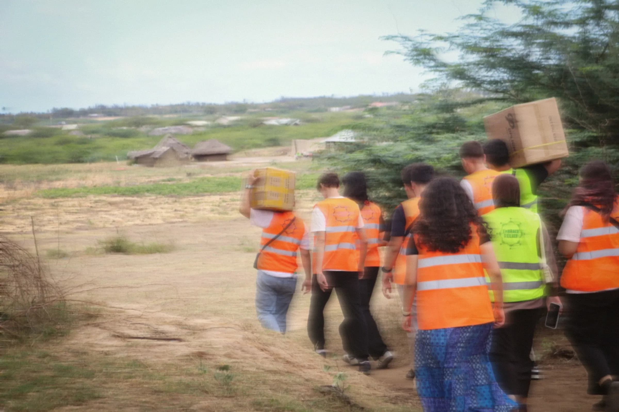 LeadUp volunteers in orange vests carry boxes of supplies along a dirt path in Kenya.